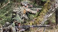 Zwei Soldaten liegen und knien mit ihrer Waffe im Wald und zielen ins Gelände.