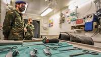 Im Vordergrund liegen medizinische Instrumente, dahinter stehen Soldaten in einem Container