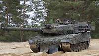Ein Kampfpanzer steht auf einer Sandfläche. Zwei Soldaten blicken aus den Luken des Panzers