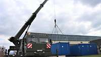 Ein Kranfahrzeug hebt einen blauen Container an.