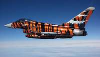 Ein Eurofighter mit dem Namen “Bronze Tiger” in kompletter Tiger-Lackierung über den Wolken.