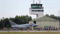 Ein Eurofighter vor einem Tower und Publikum auf dem Flugplatz.
