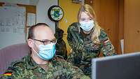 Eine blonde Soldatin und ein Soldat besprechen etwas an einem Computer