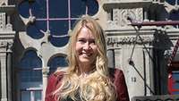 Julia Wehner Portrait für Galerie Eine blonde Frau im roten Hosenanzug vor einem historischen Gebäude