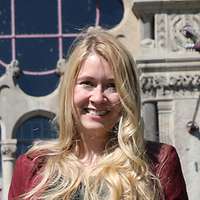 Eine blonde Frau im roten Hosenanzug vor einem historischen Gebäude