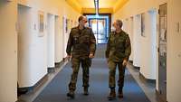 Zwei Soldaten laufen nebeneinander durch einen Gang. Beide tragen Mund-Nasen-Schutz und unterhalten sich