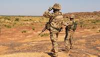 Zwei Soldaten stehen in kargem Gelände und schauen in die Ferne