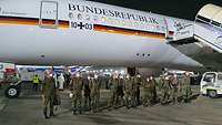 Mehrere Soldaten stehen vor einem Flugzeug. Es ist Nacht