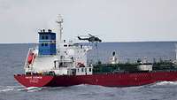 Über einem Schiff schwebt ein Hubschrauber. Aus dem Hubschrauber seilt sich ein Soldat auf das Deck des Schiffes ab