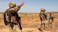 Drei deutsche Soldaten stehen im Gelände in der Wüste. Ein Soldat im Vordergrund weist mit dem Arm in eine Richtung