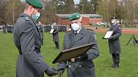 Ein Soldat überreicht eine eingerahmte Urkunde an einen anderen Soldaten.