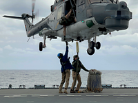 Sea-Lynx-Pilot Außenlast Zwei Personen in Uniform stehen auf dem Flugdeck. Dicht über Ihnen schwebt ein Hubschrauber.