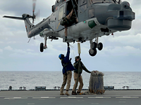 Zwei Personen in Uniform stehen auf dem Flugdeck. Dicht über Ihnen schwebt ein Hubschrauber. 