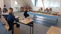 Eine Frau in Feuerwehruniform kniet vor einem Modell mit Gebäuden, das auf einem Tisch steht.