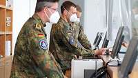 Drei Soldaten in Flecktarnuniform blicken jeweils auf einen Computerbildschirm.