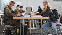 Amtshilfe Impfzentrum Rostock Wartebereich Ein Soldat in Flecktarnuniform und eine Frau in Zivilkleidung sitzen an einem Tisch und unterhalten sich.