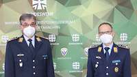 Zwei Soldaten stehen vor einer Wand mit dem grünen Polygon-Muster der Bundeswehr und tragen eine Maske.
