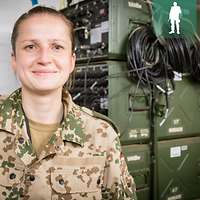 Eine Soldatin steht vor mehreren grünen Kisten mit Aggregaten, aus denen Kabel heraushängen