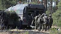 Mehrere Soldaten stehen hinter zwei gepanzerten Fahrzeugen.
