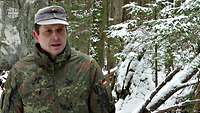 Ein Stabsoffizier steht in einem schneebedecktem Waldstück.