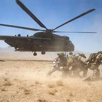 Es startet in der Wüste ein Hubschrauber CH-53 während im Vordergrund Soldaten Knien