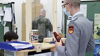 Ein Soldat steht vor einem Check-in Schalter. Dahinter sitzt eine Soldatin.