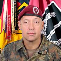 Ein Soldat schaut in die Kamera, hinter ihm die Truppenfahne.