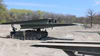 Ein Brückenlegepanzer Biber steht auf einer kahlen, sandigen Fläche.