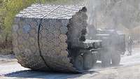 Ein Bundeswehrlaster rollt von seiner Ladefläche eine Faltstraße aus Aluminiumteilen ab.