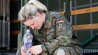 Eine erschöpfte Frau sitzt im Schatten eines Containers