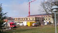 Baustelle mit eingerüsteten Rohbauten, Kran und Baustellenfahrzeugen.
