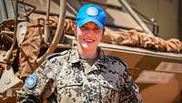 Eine Soldatin steht vor einem militärischen Fahrzeug, hält die Hände in den Hüften und trägt ein blaues Basecap