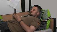 Ein Soldat liegt in seinem Bett und hört mit seinem Handy und Kopfhörern Musik