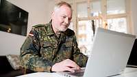 Ein Soldat in Uniform arbeitet von zuhause aus an seinem Laptop.