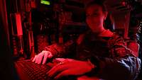 Eine Soldatin sitzt bei Rotlicht an einer PC-Tastatur in einem Fahrzeug