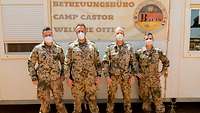 Vier Soldaten stehen vor einem Schild, auf dem „Betreuungsbüro Camp Castor“ steht. Alle Soldaten tragen einen Mund-Nasen-Schutz 