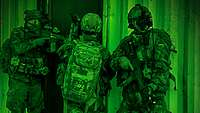 Drei Soldaten mit taktischer Ausrüstung, Waffen und Nachtsichtgeräten stehen an der Tür eines Gebäudes hintereinander.