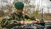 A blonde female soldier working on the engine of a cross-country vehicle