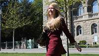 A young blonde woman in a red pantsuit walking in front of a historic building