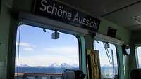 Blick aus einem Fenster einer Schiffsbrücke auf eine Küste mit verschneiten Bergen.