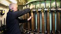 Ein Marinesoldat in blauer Arbeitsuniform stellt Granaten eines Schiffsgeschützes in ein rundes Gestell.