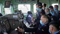 Mehrere Marinesoldaten in blauer Arbeitsuniform auf der Brücke eines Schiffes.