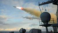 Eine Rakete mit Feuerschweif vor einem bewölten Himmel.