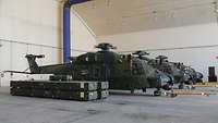 Drei Hubschrauber mit demontierten Rotorblättern stehen nebeneinander in einem Hangar