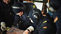 Formidable Shield 2017 Fregatte Sachsen Operationszentrale Mehrere Marinesoldaten in dunkelblauer Arbeitsuniform und dunkelblauen Stoffhauben beugen sich über eine Kladde.