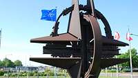 Eine Skulptur in Form eines vierzackigen Sterns; im Hintergrund Flaggen an Flaggenmasten.