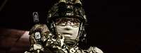 Ein Soldat in Uniform mit Schutzbrille und Gesichtsmaske hält mit beiden Händen eine Pistole.