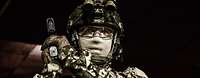 Ein Soldat in Uniform mit Schutzbrille und Gesichtsmaske hält mit beiden Händen eine Pistole.