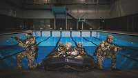 Soldaten in Uniform stehen mit einem Schlauchboot in einer Schwimmhalle.