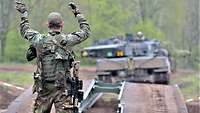 Ein Soldat unterstützt mit Handzeichen den Kampfpanzer beim Überqueren einer Brücke.